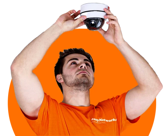 Engineer in orange easyNetworks shirt with both arms raised up servicing a ceiling mounted cctv camera.